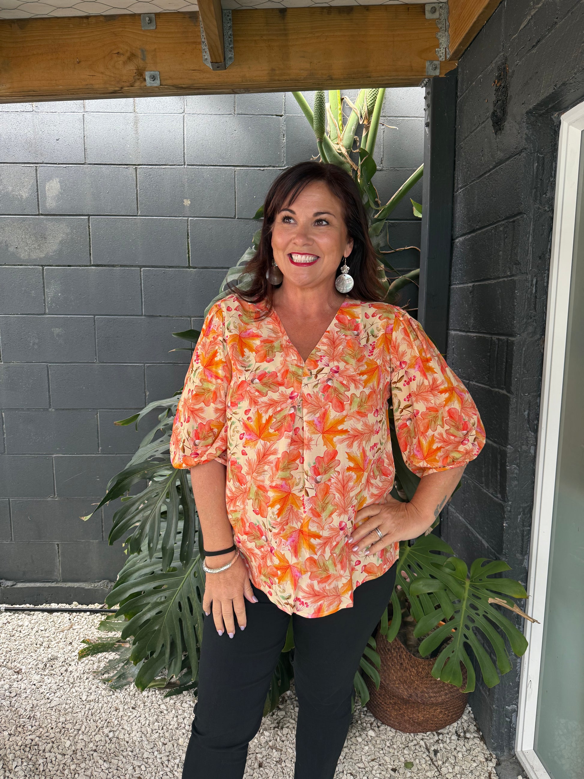Woman in a colorful floral shirt standing on a tiled floor with plants around.