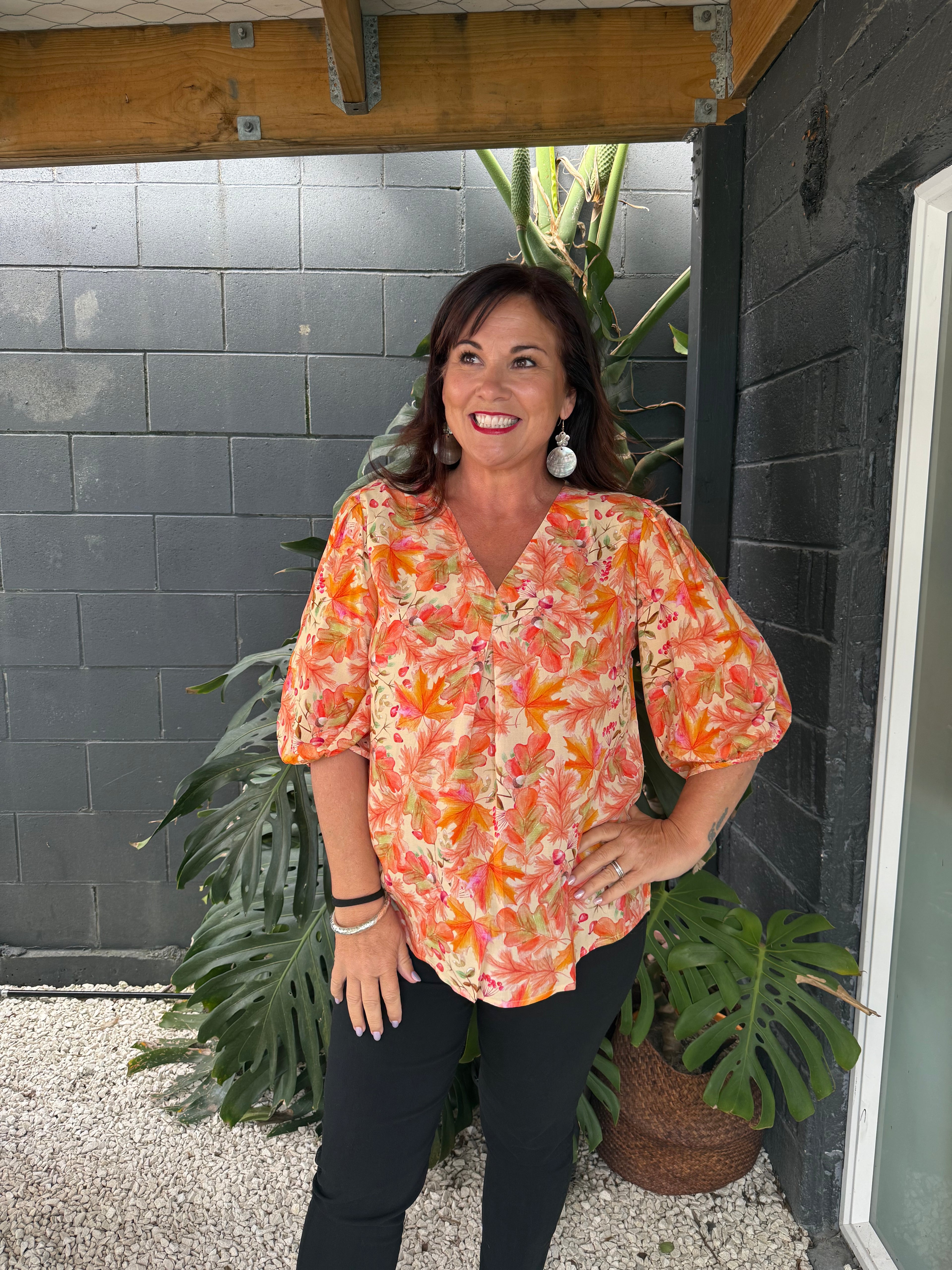 Woman in a colorful floral shirt standing on a tiled floor with plants around.
