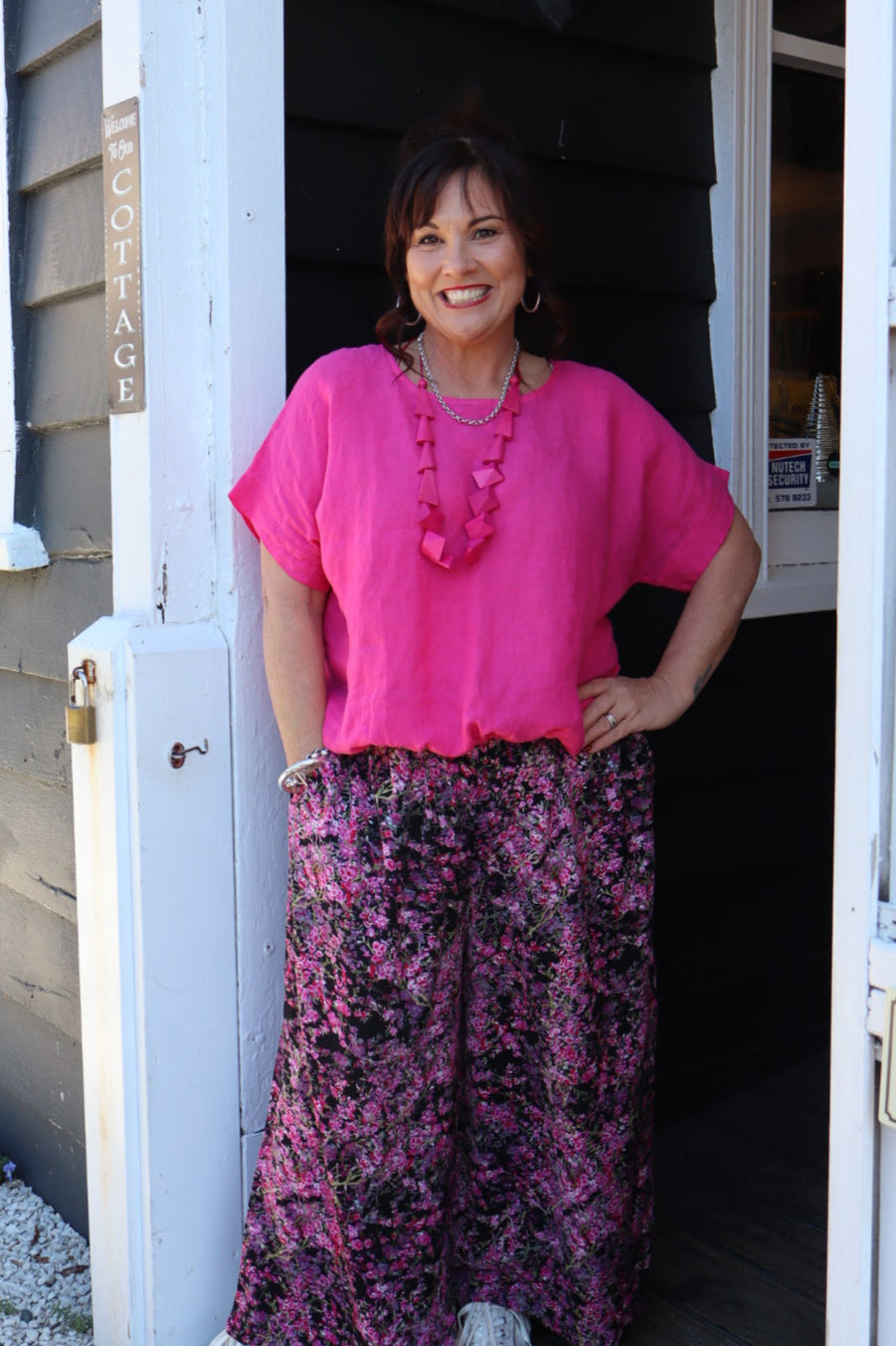 Person wearing a pink top and purple floral pants standing on a wooden deck.