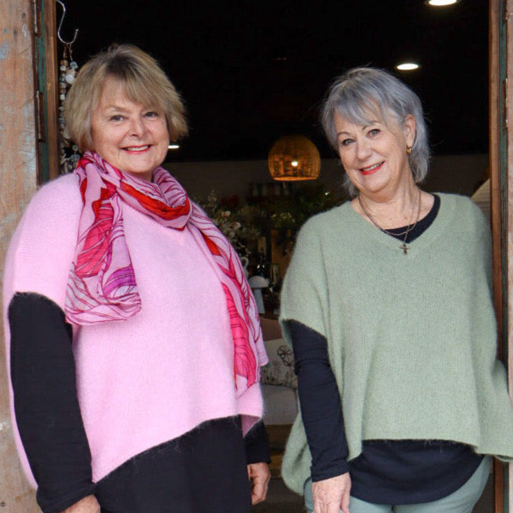 Two women standing in a doorway, one holding a black handbag and the other a beige handbag.